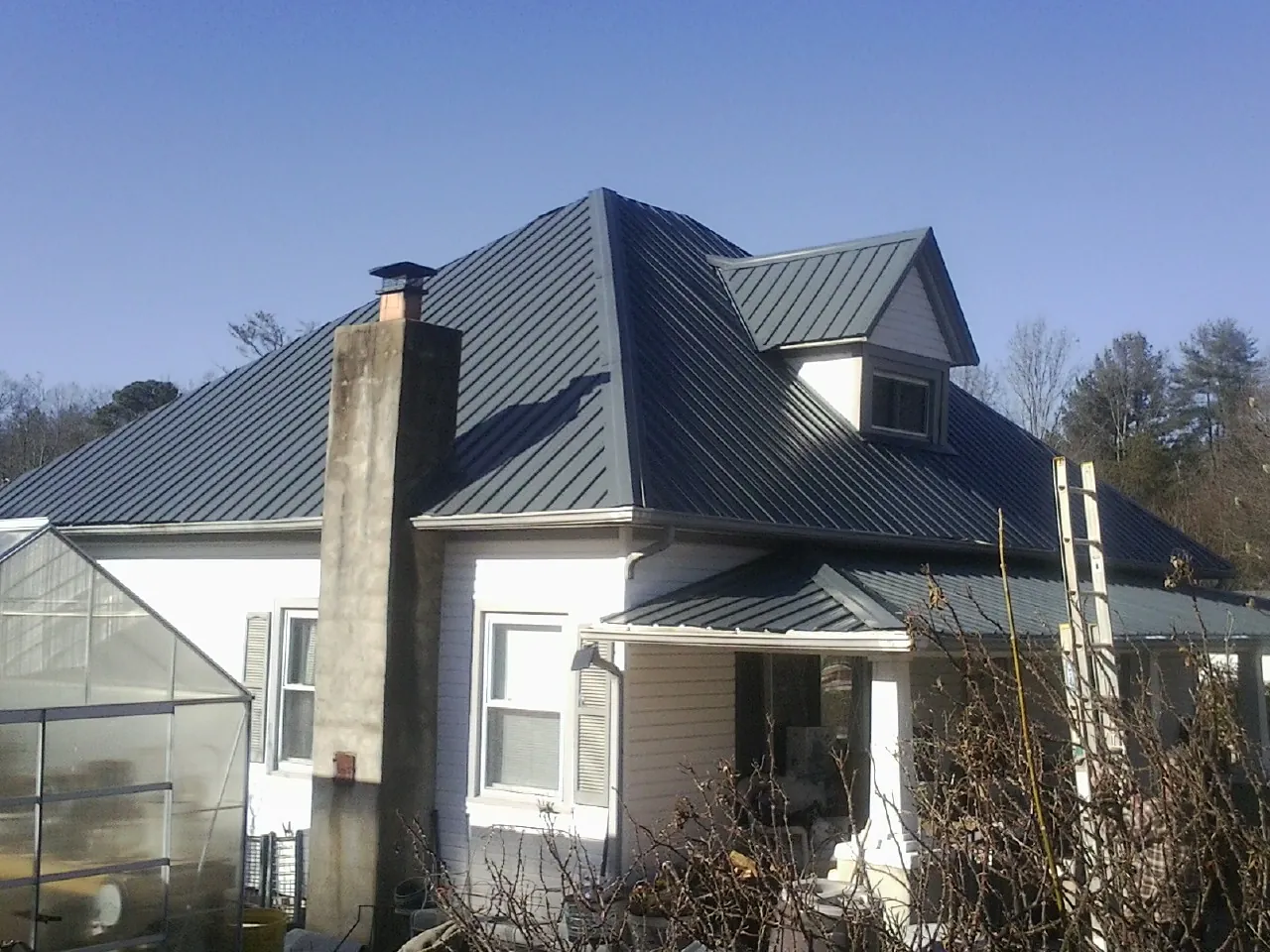 Dark blue standing seam metal roof on a white farmhouse with dormer — Slate & Tile Roof Repair by Roofing Brothers in Laurinburg