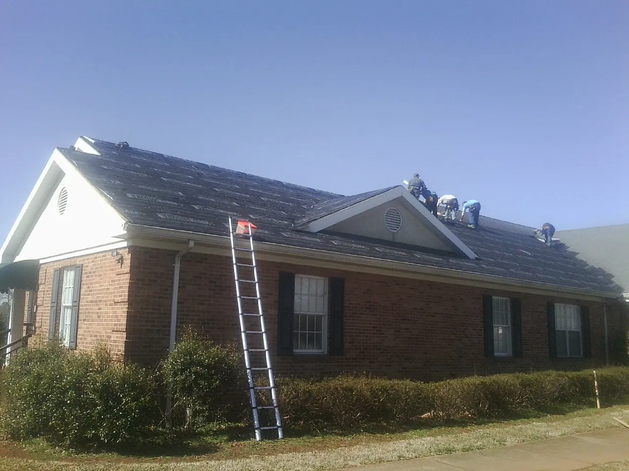 Crew tearing shingles off a brick ranch roof with a ladder set — Emergency Roof Repair work by our crew in Laurinburg