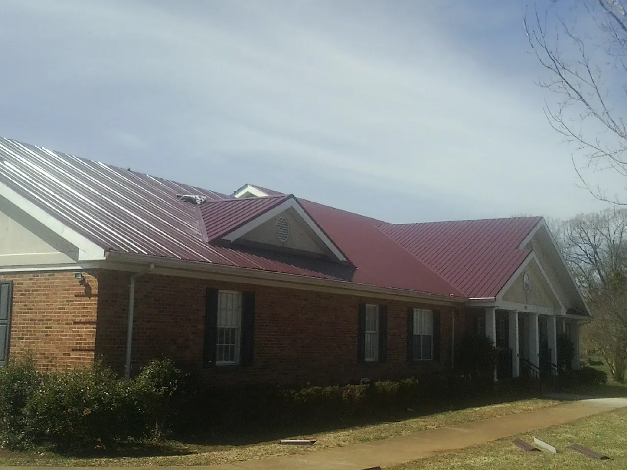 Red metal roof with gabled entries on a long brick building, from a Hail Damage Roof Repair job in Laurinburg