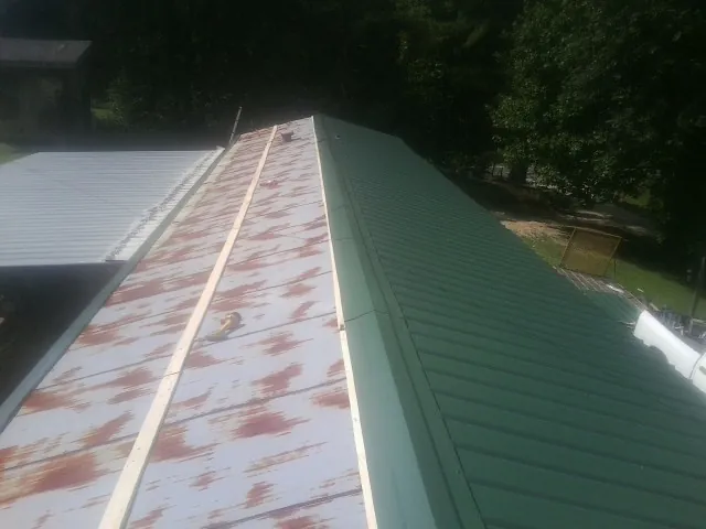 Old rusted panels beside newly installed green metal roofing — Wind Damage Roof Repair by Roofing Brothers in Laurinburg