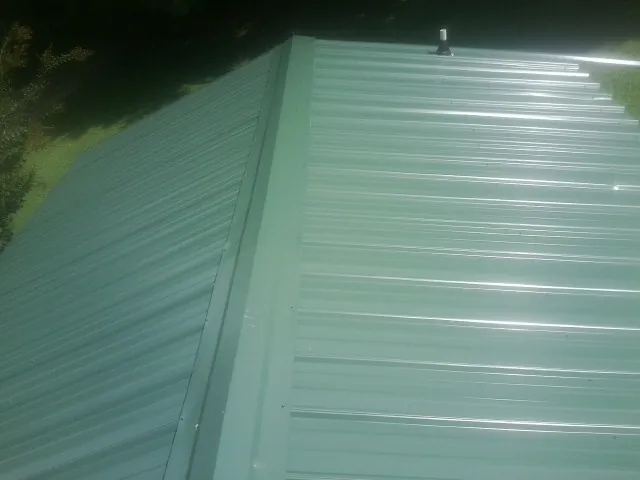 New green metal panels meeting at the ridge of a roof — Flat Roof Repair work by our crew in Laurinburg