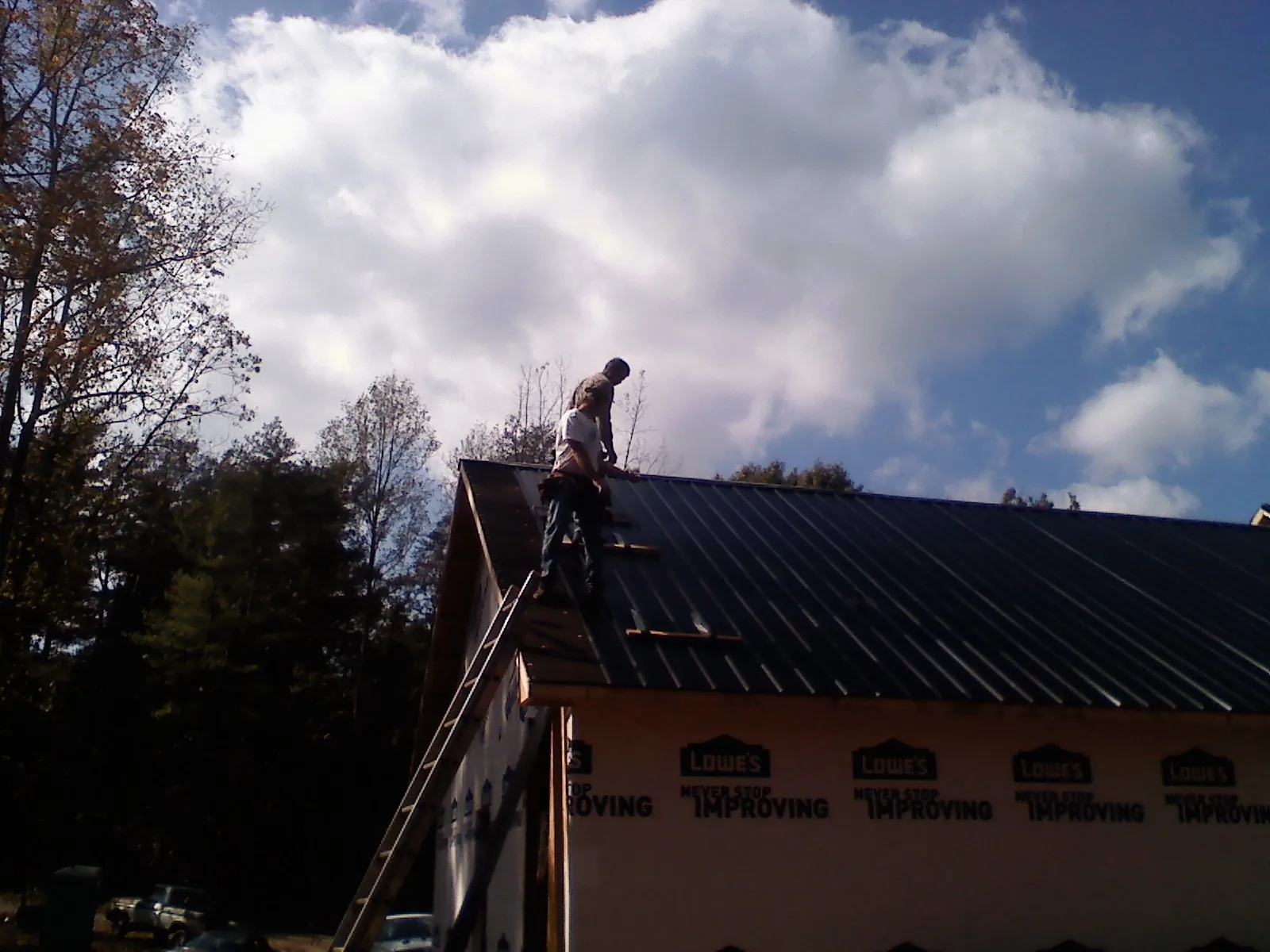 Roofer fastening dark metal panels high against a cloudy sky, from a Roof Inspection job in Laurinburg
