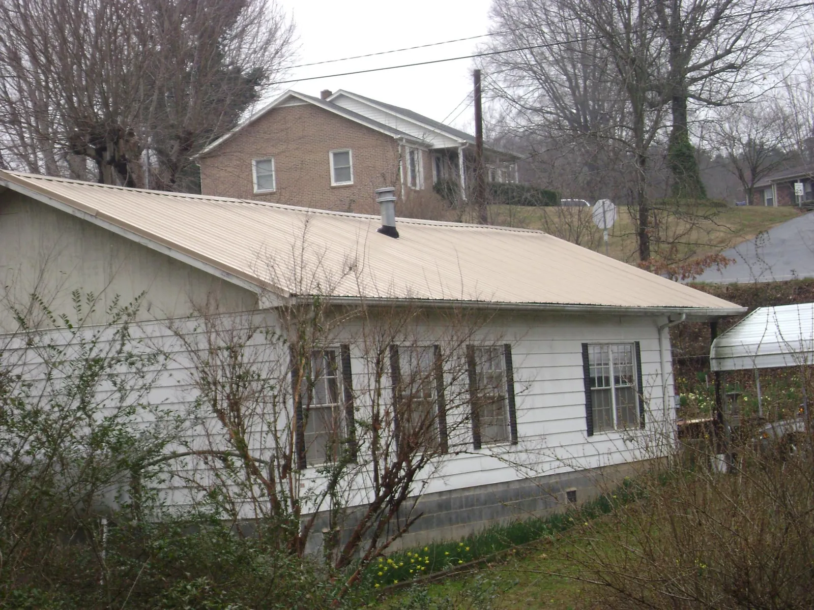 Tan metal roof on a white sided house set into a hillside — Commercial Roofing by Roofing Brothers in Laurinburg