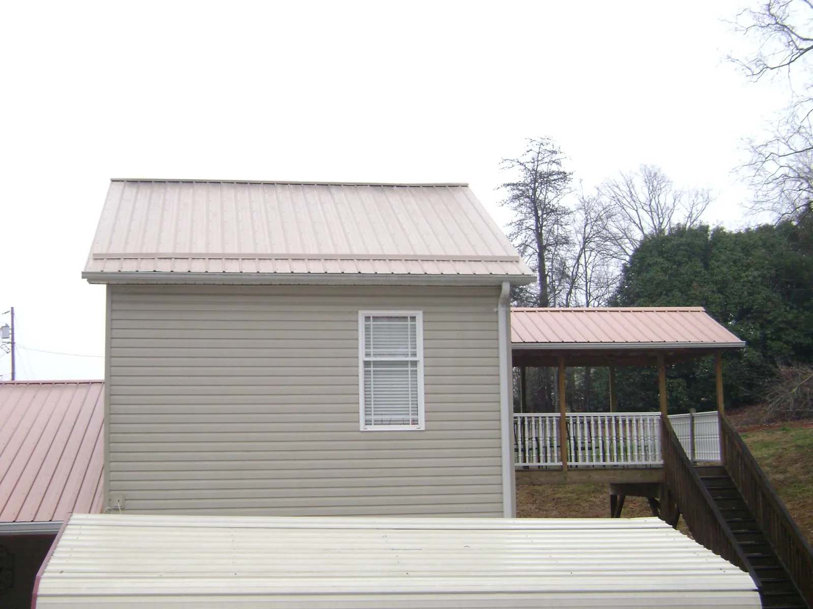 Tan metal roofs on a two story addition and attached porch, from a Roof Replacement job in Laurinburg